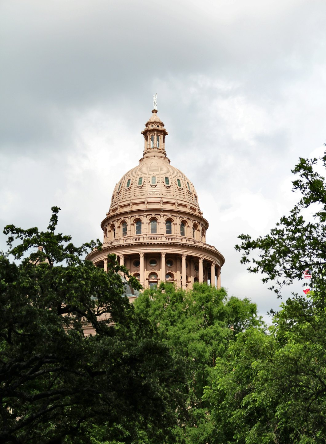A pink granite capitol dome stands behind lush green trees.